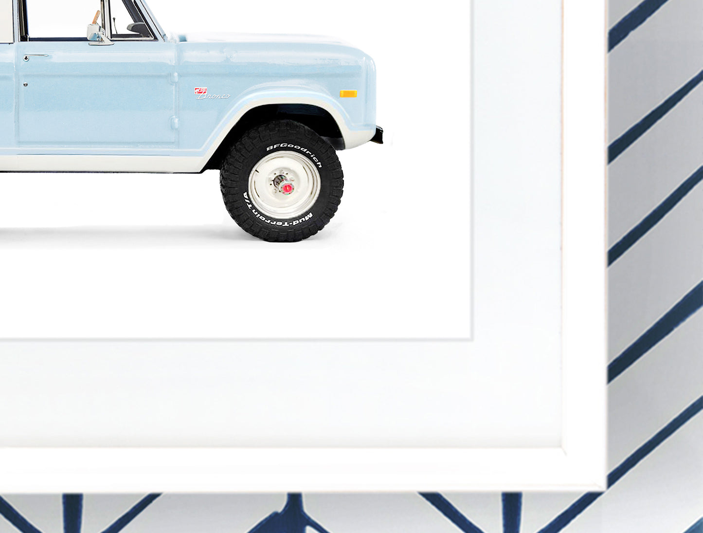 Close-up detail of a framed vintage Ford Bronco art print, showing the crisp white frame, high-quality matte paper texture, and the light blue paint detail of the classic 4x4.