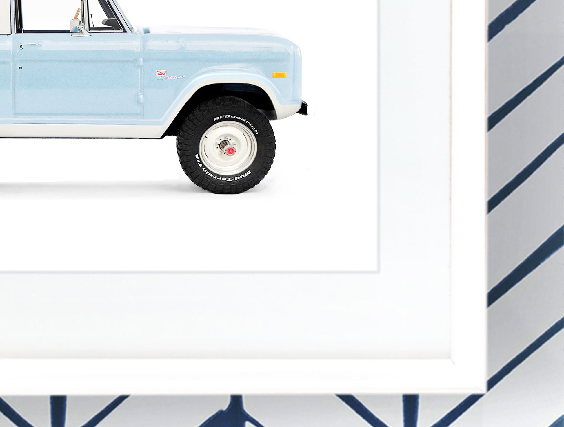 Close-up detail of a framed vintage Ford Bronco art print, showing the crisp white frame, high-quality matte paper texture, and the light blue paint detail of the classic 4x4.